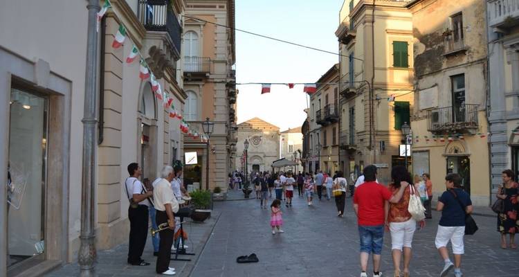 Una calle concurrida con gente caminando, bordeada de edificios y banderas.