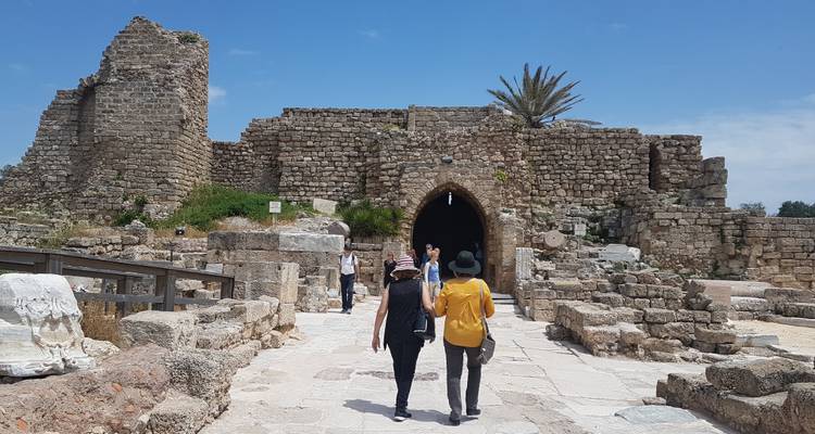 Des touristes marchent vers une entrée historique en pierre par une journée ensoleillée.
