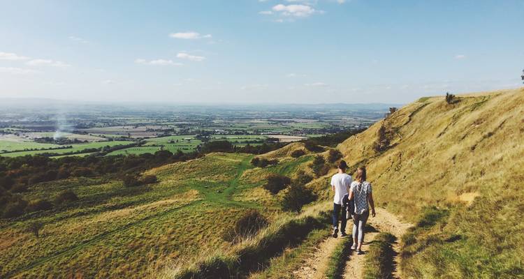 Deux personnes marchant sur un sentier de colline surplombant une vallée.