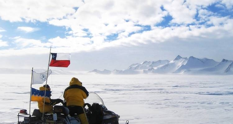 Zwei Entdecker auf Schneemobilen in einer weiten verschneiten Landschaft mit Flaggen.