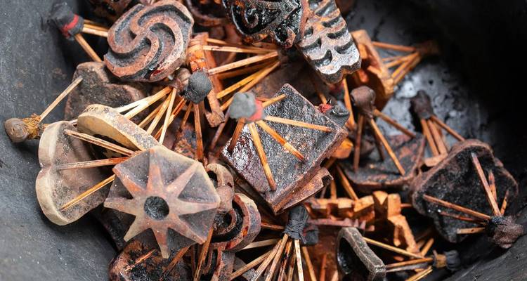 Pila de sellos de madera tallados Adinkra cubiertos en tinte oscuro, mostrando patrones simbólicos y palos.