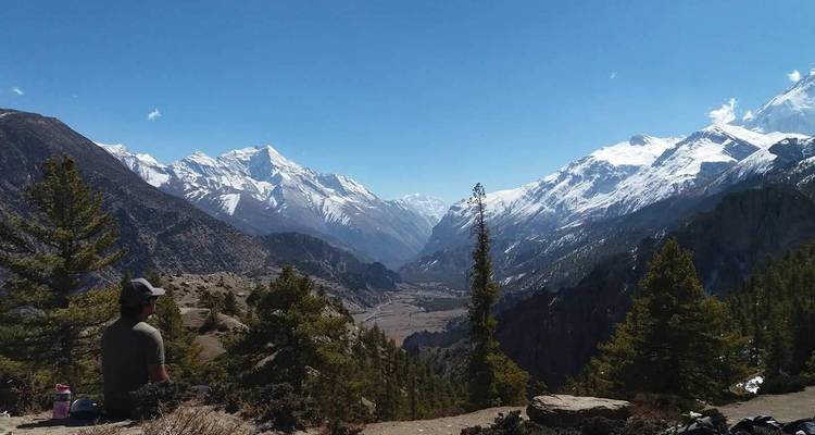A lone hiker sitting, admiring the view of vast snowy mountains.