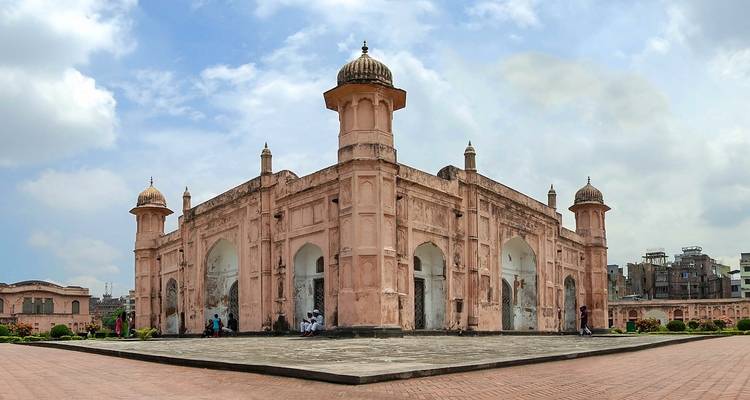 Une mosquée couleur saumon avec des dômes dans un cadre de jardin.