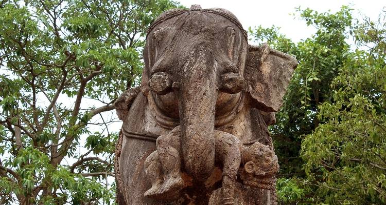 Stone sculpture of an elephant with trees behind.