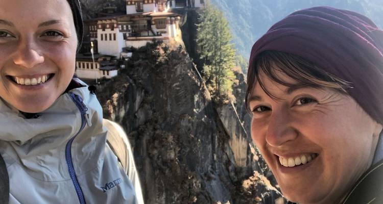 Zwei Frauen lächeln mit dem Paro Taktsang Kloster im Hintergrund.