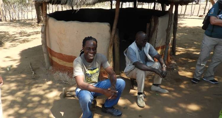 Zwei Männer sitzen an einem sonnigen Tag in der Nähe einer traditionellen Hütte.