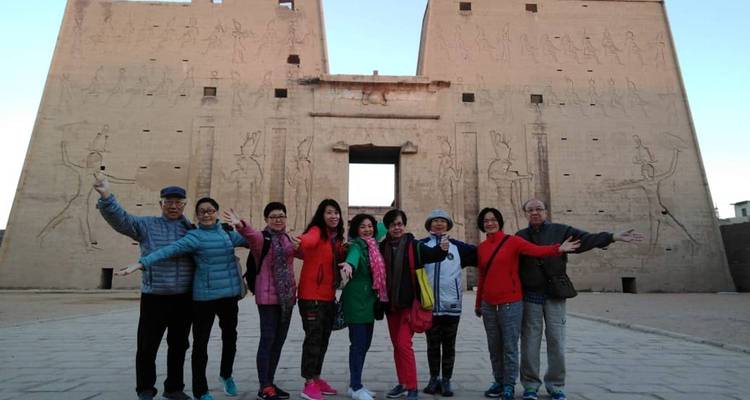 Un grupo de turismo posa alegremente frente a un gran templo antiguo egipcio con relieves tallados.
