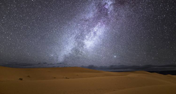 Starry night sky over sand dunes with Milky Way visible.