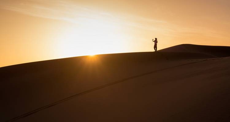 A person standing on a sand dune at sunset.
