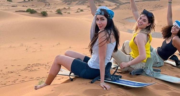 Young women sitting on sandboards in the desert, celebrating.