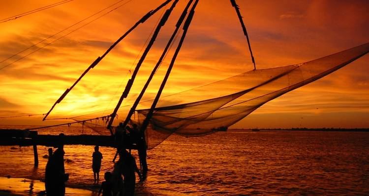 Silhouettes of people with fishing nets against a vibrant sunset over water.