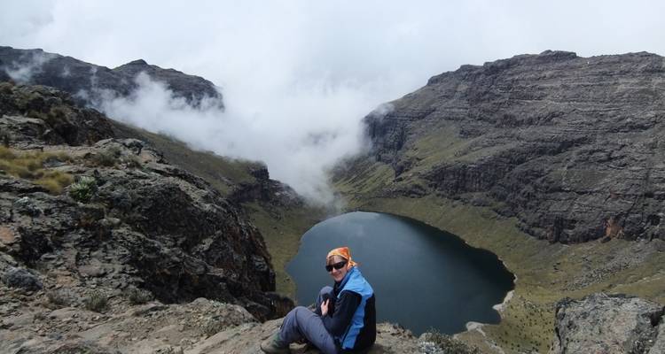 Persoon zittend op kliprand met uitzicht op meer en bergen.