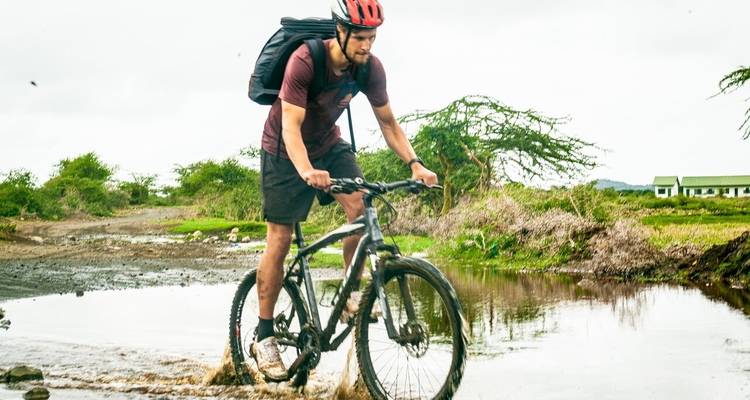 Man cycling through a wet path with nature surroundings.