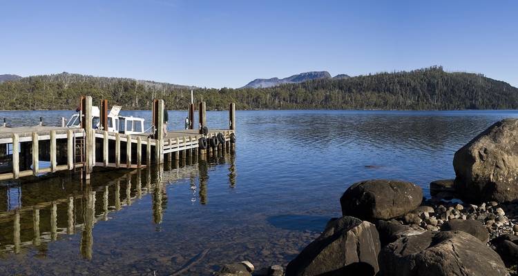 Petit ponton en bois s'étendant dans un lac cristallin entouré de collines boisées en Tasmanie