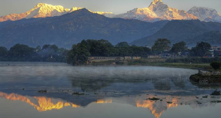 Snow-capped mountains reflecting on a lake during sunrise.