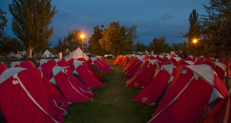 Un camping avec des rangées de tentes rouges illuminées la nuit.