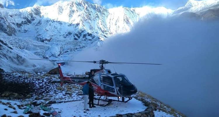 People with a helicopter against a backdrop of snowy mountains.