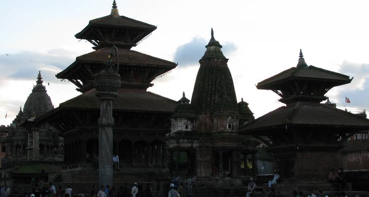 Templos con tejados de pagoda recortados en silueta y visitantes en una plaza histórica nepalí contra un cielo brillante.