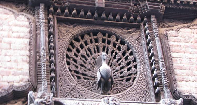 Ventana de pavo real de madera tallada con intrincados detalles, ubicada dentro de un antiguo muro de ladrillos.