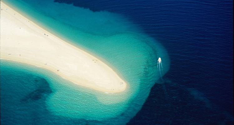 Vista aérea de una playa de arena y aguas azules cristalinas.