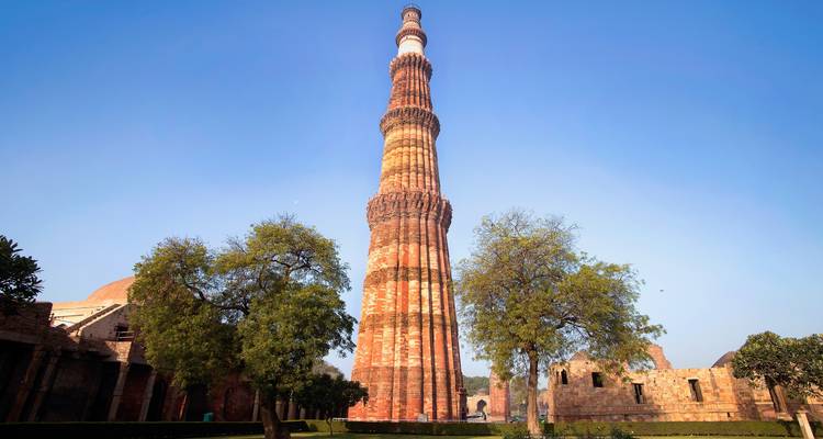 El Qutb Minar rodeado de árboles en un día soleado.
