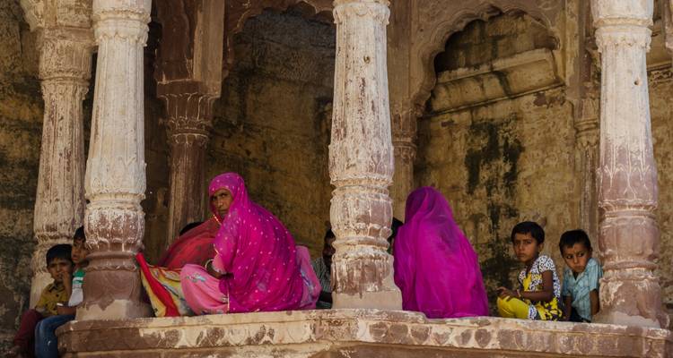 Mujeres y niños con ropa tradicional sentados en un arco.