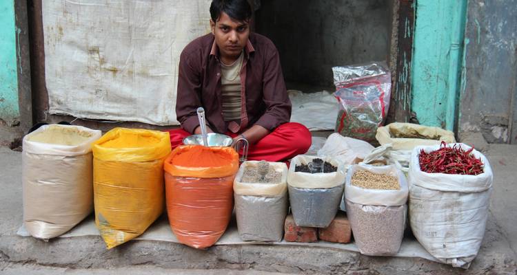 Hombre vendiendo varias especias en sacos coloridos en una calle.