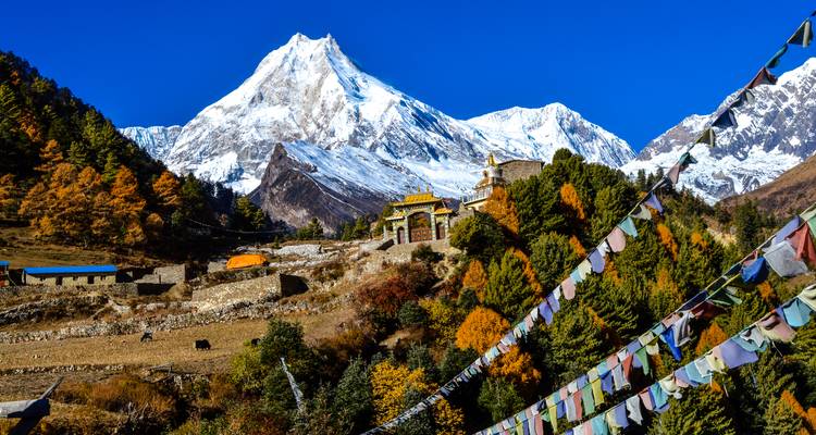 Snow-covered mountain and a Buddhist monastery with prayer flags.