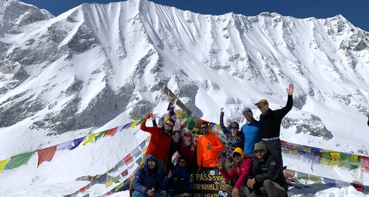 Group of people posing with prayer flags and snowy mountains behind.