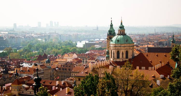 Verhoogd uitzicht over de terracotta daken van Praag richting de Sint-Nicolaaskerk en verre bruggen.
