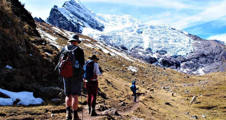 Wandelaars op een pad met besneeuwde bergen op de achtergrond.