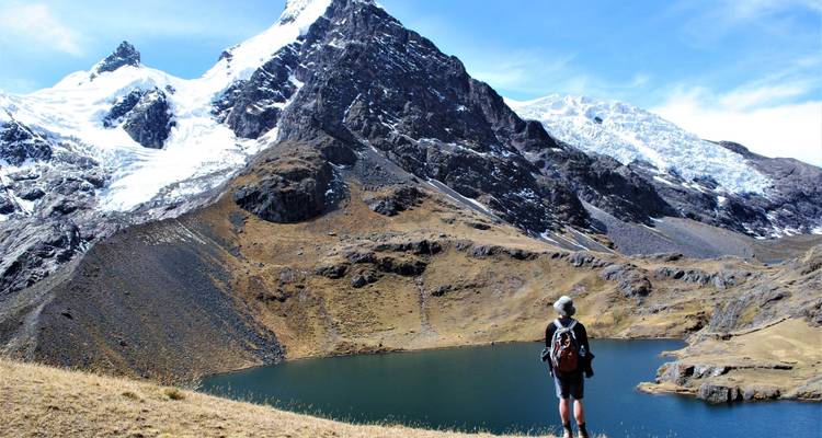 Persoon die bij een meer staat met besneeuwde bergen op de achtergrond.
