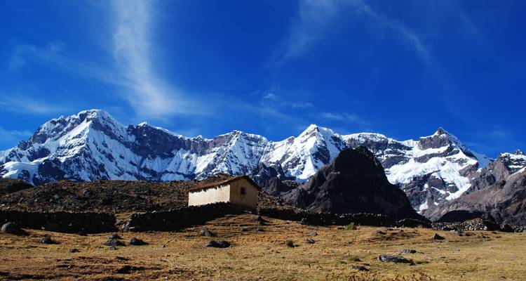 Een rustiek huis in een uitgestrekt berglandschap met besneeuwde toppen.