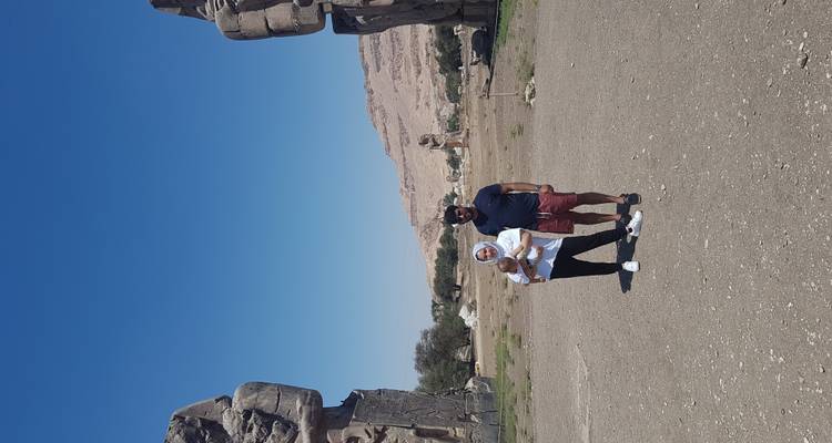 Toeristen die poseren tussen twee gigantische beelden met woestijnlandschap.