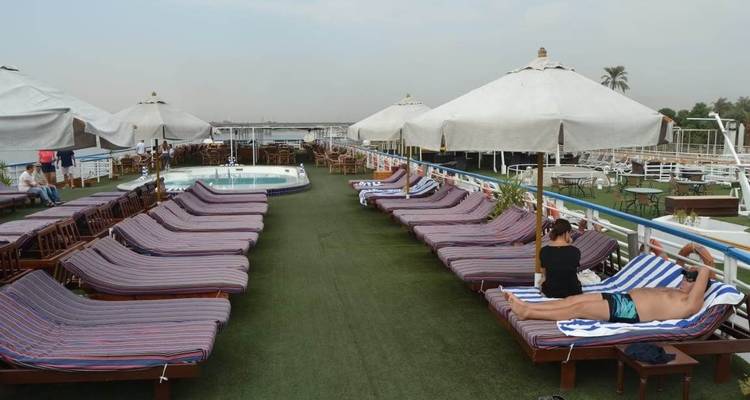 Ligstoelen en parasols op een scheepsdek met mensen die ontspannen.