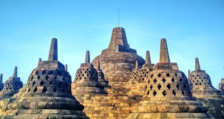 Temple de Borobudur avec des stupas au premier plan sous un ciel bleu dégagé.