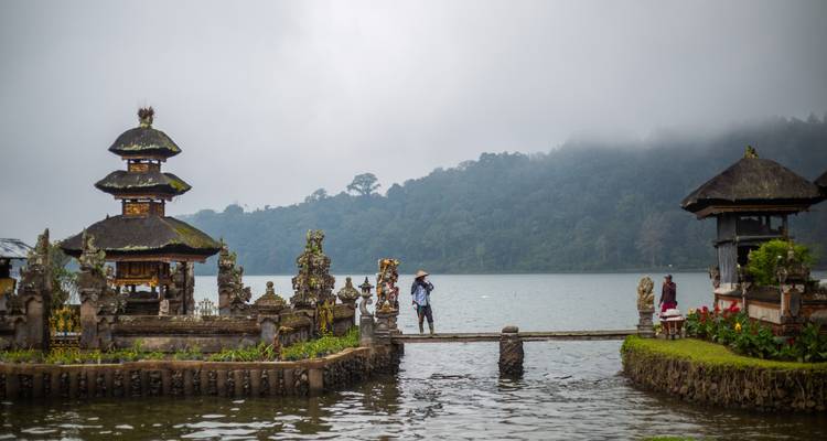 Temple traditionnel au bord d'un lac avec une personne marchant sur un pont.