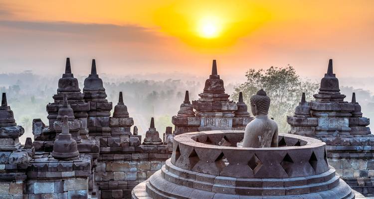 Sonnenaufgang über den Stupas des Borobudur-Tempels mit warmem orangefarbenem Himmel und nebligem Wald darunter