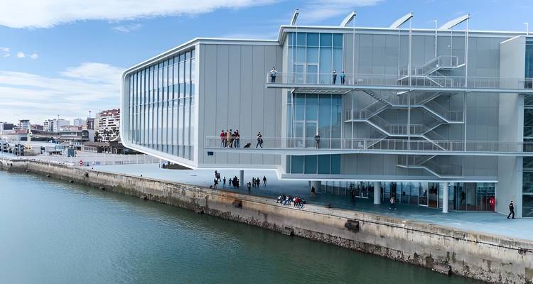 Un edificio arquitectónico moderno junto al agua con personas caminando alrededor.
