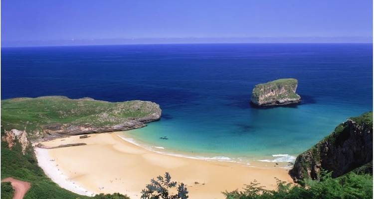 Plage de sable avec eau turquoise et falaises rocheuses.