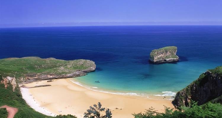 Een ongerept strand met helder blauw water en een klein eiland in de verte.