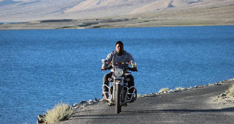 Persona montando una motocicleta en la carretera junto a un lago.