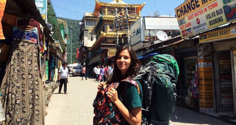 Mujer joven con mochila en un pueblo concurrido con un edificio estilo pagoda.