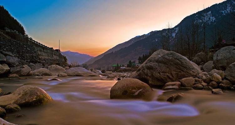 Un río tranquilo al atardecer con montañas al fondo.