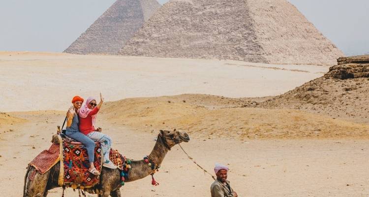 Zwei Menschen auf einem Kamel vor den Pyramiden.