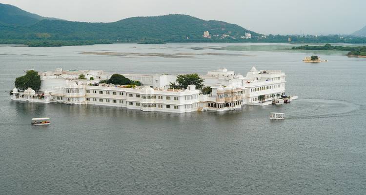 Un bâtiment blanc semblable à un palais entouré d'un lac et de verdure.