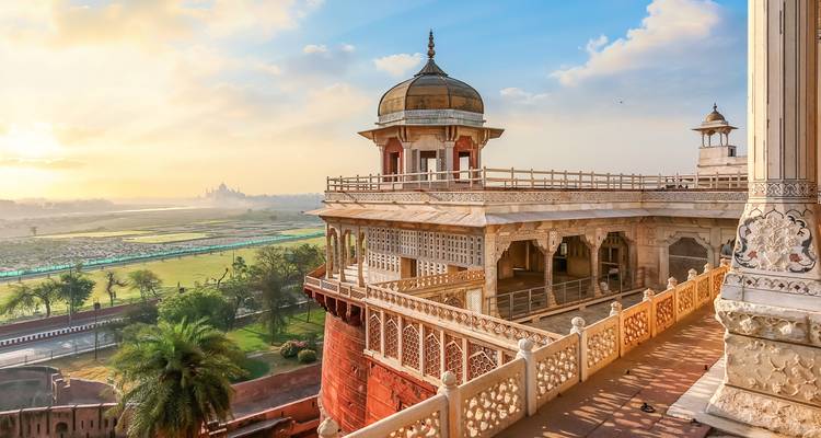 Gouden zonsopgang boven het sierlijke Mughal-balkon van het Agra Fort met de Taj Mahal zichtbaar in de verte.