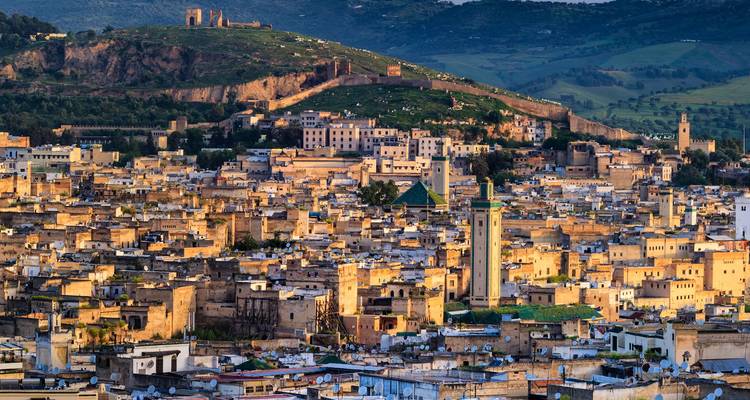 Uitgestrekt zonsondergangzicht over Fes medina met gouden muren, minaretten en een heuveltopvesting.