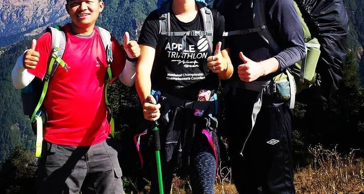 Drie wandelaars poseren met duimen omhoog in een bergachtig gebied.