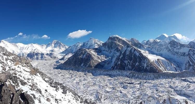Panoramic view of snow-covered mountain range under a bright blue sky.